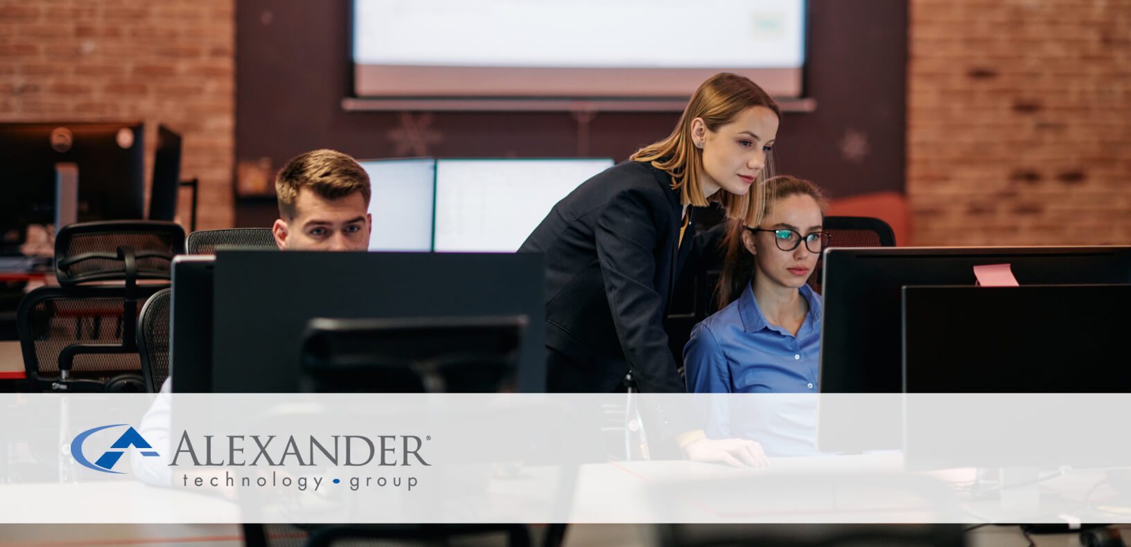 a woman stands over colleages at computers helping them with their work