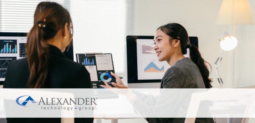 Here's suggested alt text for the image on this page: Concise version: "Two women collaborate at a desk reviewing data charts on computer monitors and a tablet in a modern office.
