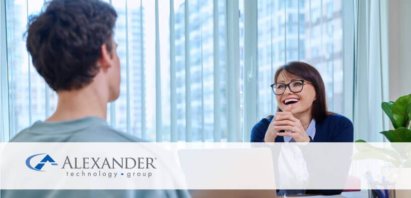A woman sitting with her computer smiling and talking to a man