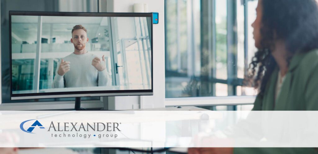 A woman looking at a computer with a video of a man talking on the screen