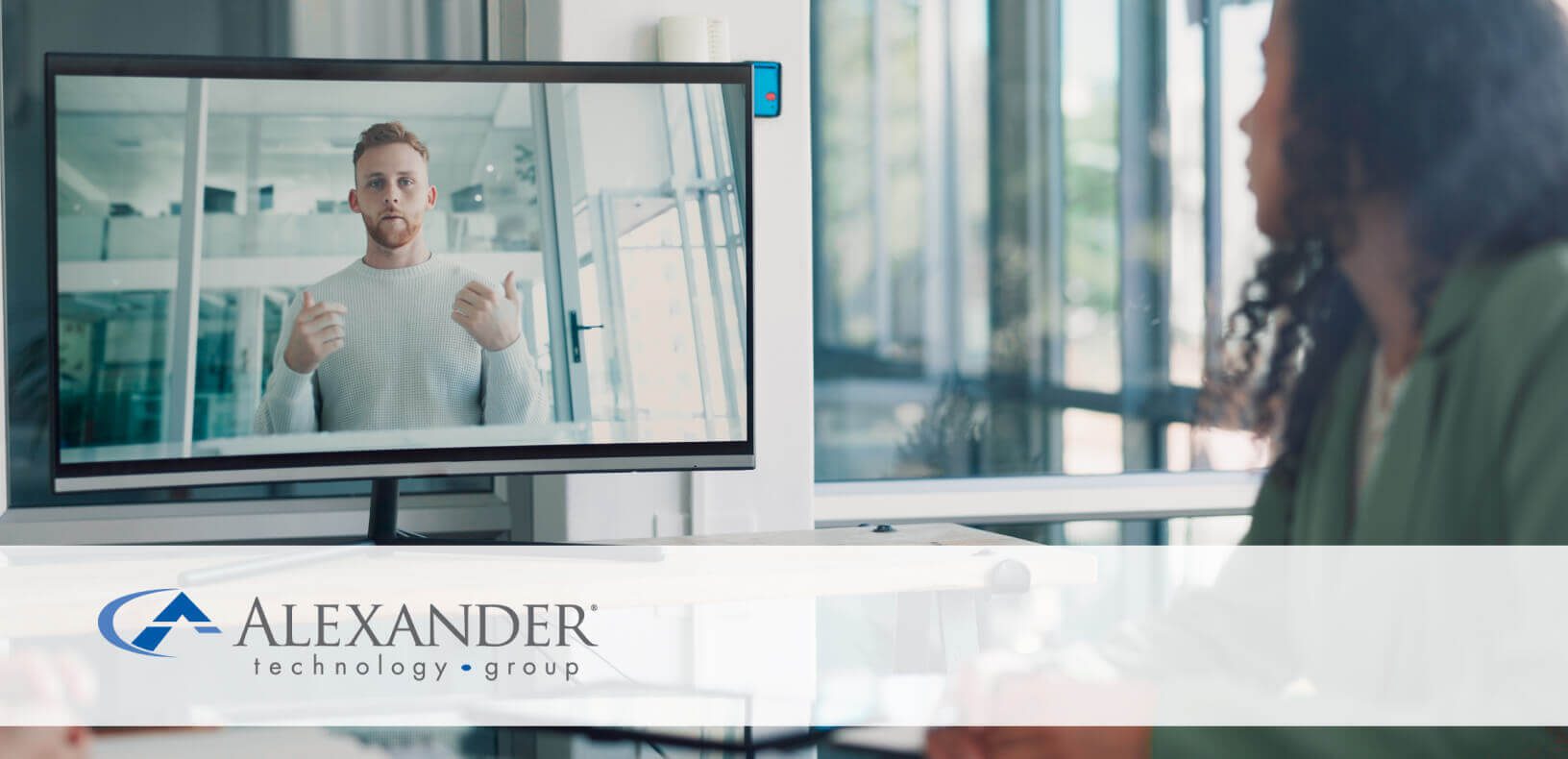 A woman looking at a computer with a video of a man talking on the screen